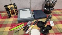 Full view of lot showing various BBQ tools, spice package, cutting board, and apron on a checkered tablecloth