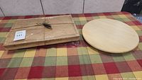 The butcher block cutting board placed next to the round wooden lazy susan on a checkered fabric surface
