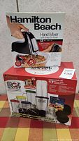 Photo showing both Hamilton Beach Hand Mixer box and Magic Bullet 17-piece set box stacked together.