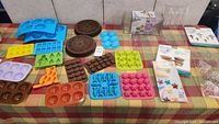 Wide shot showing variety of silicone and plastic molds including blue half-sphere molds, brown cookie molds, yellow Lego molds, pink and orange molds, and clear packaging.