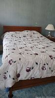Bed with floral patterned quilt and wood frame with headboard. Nightstand and lamp visible in background.