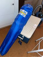 Photo of blue cooler on floor with folding camp chair sleeve resting on top, by laundry room machines.
