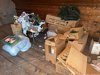Multiple cardboard boxes and loose packaging containing ornaments and faux pine branches in attic space