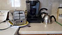 Photo showing the Keurig coffee maker, two kettles, and Hamilton Beach toaster on a kitchen counter.