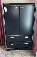 Front view of the black highboy wardrobe with two doors and three drawers, showing gold handles and trim detail.