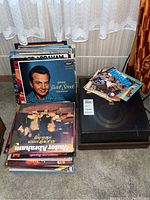 Wide view of Panasonic record player with vinyl records stacked around it, showing album covers and 45 rpm record sleeves on top.