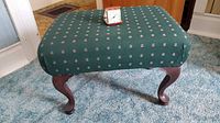 Foot stool upholstered in green fabric with small floral pattern, wooden cabriole legs visible, photographed indoors on a blue carpet.