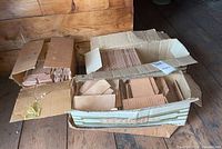 Three open cardboard boxes filled with terracotta color ceramic tiles of different sizes placed on a wooden floor against a wooden wall