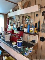 Wide view of workshop bench with assorted tools, toolboxes, paint containers, and other hardware items on and above the bench.