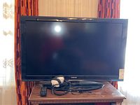 Front view of the Toshiba 39-inch TV on a round black stand with remote and headphones visible on the stand.