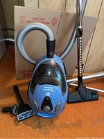 Full view of blue Dirt Devil Purpose canister vacuum with connected hose and three attachments visible laid out on floor.