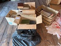 Boxes of vintage books and magazines, plastic bag partially visible, all placed in attic space on wooden floor