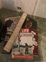 Photograph showing vintage magazines including Chums, Life with JFK, and another Life magazine with a crowd, alongside a rolled map.