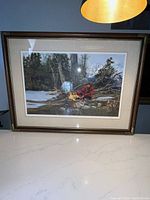 Framed vintage print showing a winter scene with trapper by fire, in good condition with visible details of frame and matting.