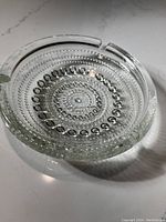 Angled side perspective showing the ashtray's depth and detailed raised bead pattern in concentric circles with three ash rests on rim.