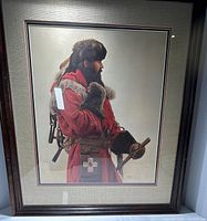 Framed print of a mountain man in fur and red coat, signed by James Bama, titled "Winter Trapping".
