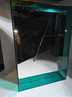Front view of the Kartell Only Me square wall mirror showing the reflective surface and transparent teal frame.