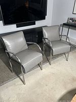 Pair of gray vintage club chairs with chrome frames placed in front of a black console and TV.