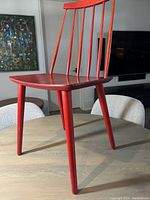 Side view of the red Scandinavian Stick Back chair showing the seat, legs and back spindles.