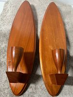 Pair of Mid Century Modern teak wood wall sconces each with oval backplate and single taper candle holder, photographed from above on a grey textured surface.