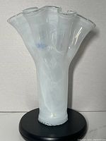 Full view of the Murano white swirl handkerchief vase on a black base showing free form shape and crystal top edge.