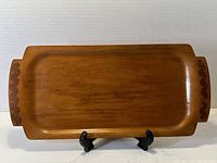 Front of rectangular walnut bentwood serving tray showing the smooth finish, raised edges, and geometric scallop cut out handles.