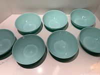 Top down view showing six robin's egg blue bowls arranged in two rows of three on a white surface.