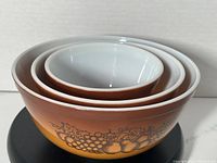 Photo showing all three nesting vintage Pyrex Old Orchard mixing bowls stacked inside each other, highlighting the white interior and brown fruit patterned exterior.