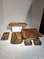 Full set of teak boards and bowls displayed on a marble surface with varying shapes and sizes.