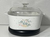 Full view of white square casserole dish with floral basket design and glass lid.