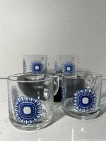 Front view showing four stackable clear glass mugs with blue sunflower design on the side.
