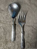 Full view of a large silver plated serving spoon and fork showing the textured renaissance pattern on the handles.