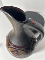 Close-up photo showing the top opening, handle, spout, and portions of the decorative diamond pattern with red dot accents on the dark bronze pottery pitcher.