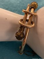 Close-up photo showing the detailed ornate textured caps and solid rolled rose gold bangle with crossover design.