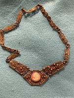 Full view of antique brass necklace with three main filigree panels and central cameo stone showing detail.