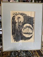 Framed black and white print featuring a haloed figure and buildings, signed by Vana Gaedehan included in the bottom right corner.