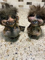 Front view of two vintage Norwegian troll figurines with distinctive facial features and fuzzy hair, placed on a speckled countertop.