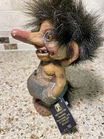 Full side view of vintage Norwegian troll figurine with shaggy black hair and detailed face, showing original tag.
