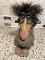 Front view of vintage original Norwegian troll figurine with wild black fuzzy hair, large nose, winking eye, and sad face expression.