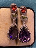 Close-up of pair of multi-colored stone earrings on cream velvet jewelry box interior.
