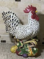 Front view of colorful ceramic rooster statue with detailed vegetable base on kitchen countertop.