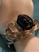 Angle view of the cuff bracelet showing the carved black obsidian Buddha head set in silver with surrounding colored gemstones.