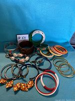 Lot of vintage bangles and bracelets displaying different materials, colors, and styles including floral designs, gold-tone, and pearl-like beads.
