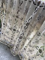 Full draped view of the cream-colored vintage table cloth showing the embroidered and crocheted floral pattern with details of the scalloped edges.