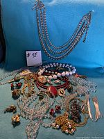 Mixed vintage jewellery lot with multiple necklaces, bracelets, earrings, and rings, displayed on a blue felt background.