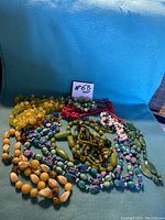 Full view of nine assorted vintage bead necklaces in various colours and sizes on blue background