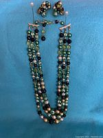 Full view of the three-strand bead necklace paired with matching clip-on earrings on a blue background