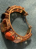 Photo of gold-tone Juicy Couture bracelet showing large amber, black, orange, and light pink stones with attached safety chain.