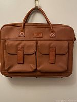 Front view of tan leather messenger bag showing two front flap pockets with closures and top handles