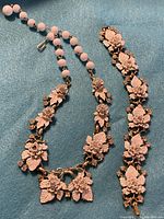 Photo of vintage necklace and bracelet set with enamel floral designs on blue background.